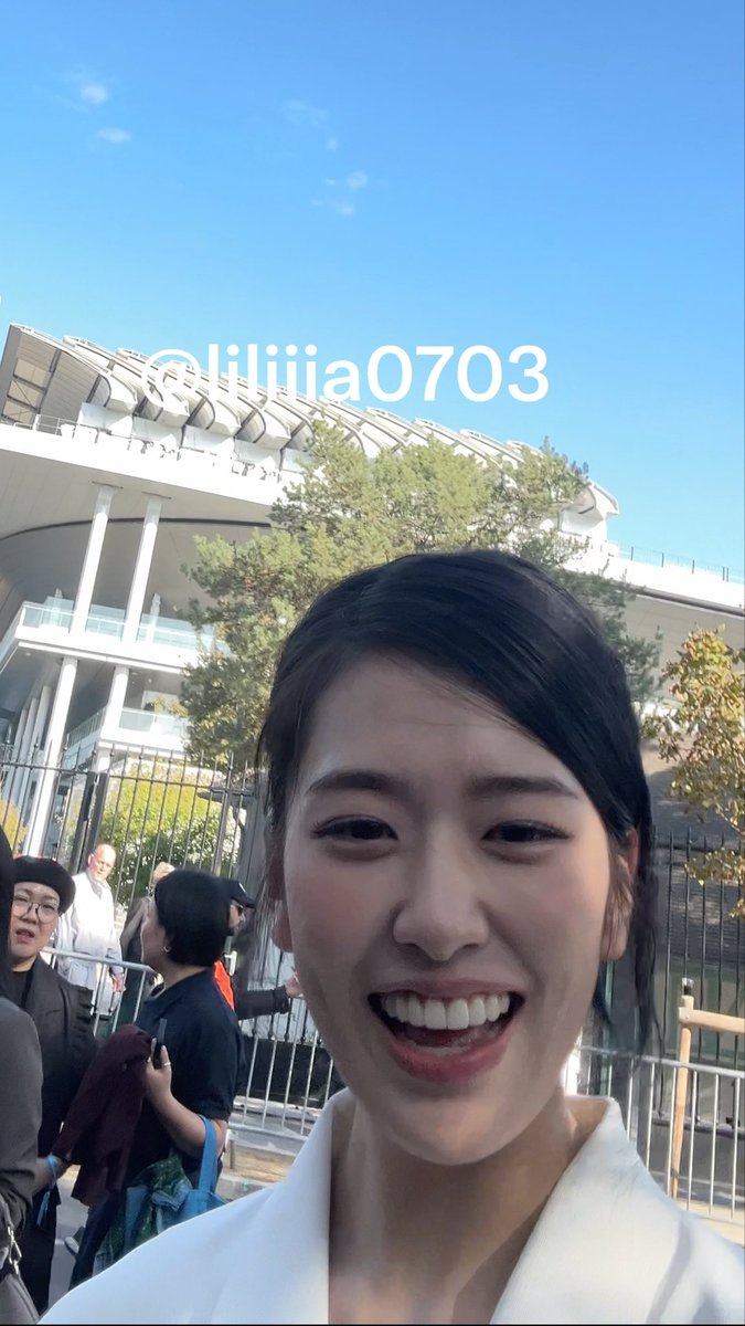 A selfie of a smiling young woman in front of a stadium, with the text "@liliiia0703" overlaid near the top of the image.