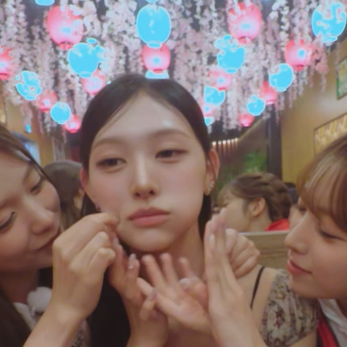 A young woman sits center frame, having her cheeks playfully pinched by two friends on either side of her, with whimsical animated blue and pink bubble-like icons decorating the scene around her face. The cute, affectionate interaction between the friends matches the post's playful "Mochi Princess" theme, capturing a sweet, squishable moment that the caption adorably celebrates.