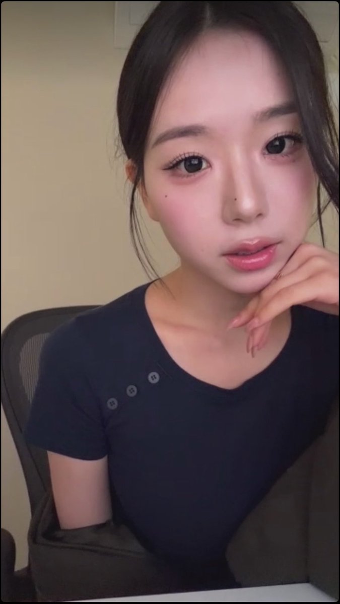A selfie of a young woman with dark hair wearing a navy blue top, resting her chin on her hand.