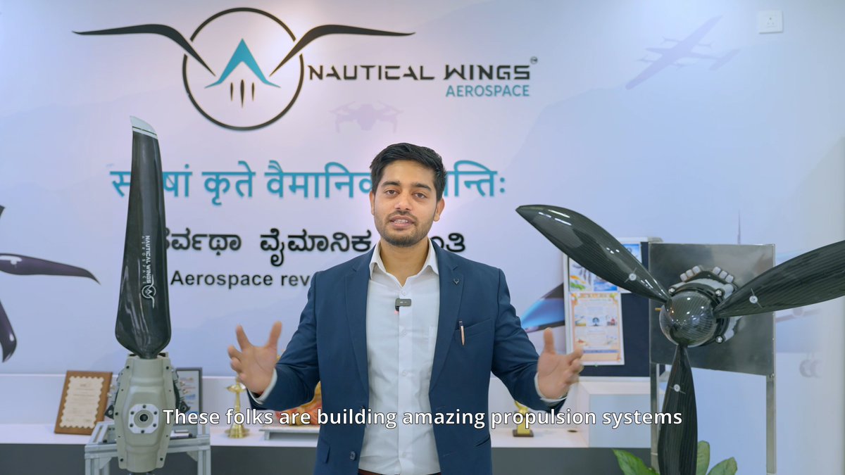 A man in a blue blazer stands between two aviation propulsion models in front of a 'NAUTICAL WINGS AEROSPACE' logo with Hindi and Kannada text, with subtitles reading 'These folks are building amazing propulsion systems'.