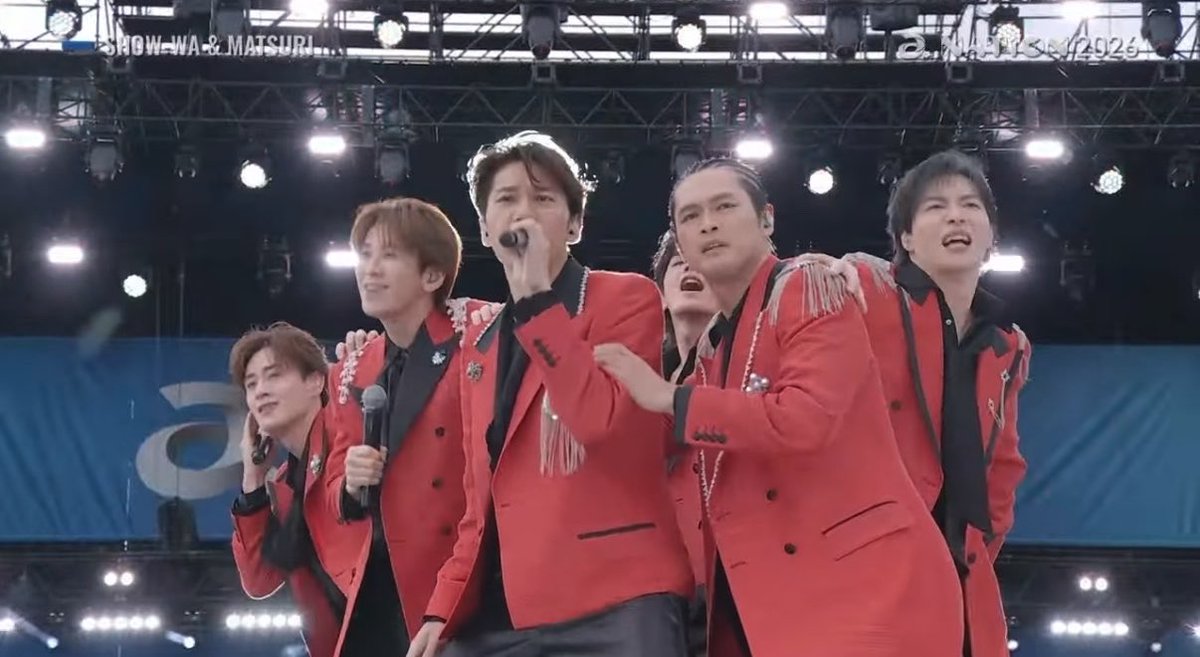 Five male performers in matching red jackets performing on a brightly lit stage, with text 'SHOW-NA & MATSURI' and '2.MATSURI 2025' partially visible at the top.