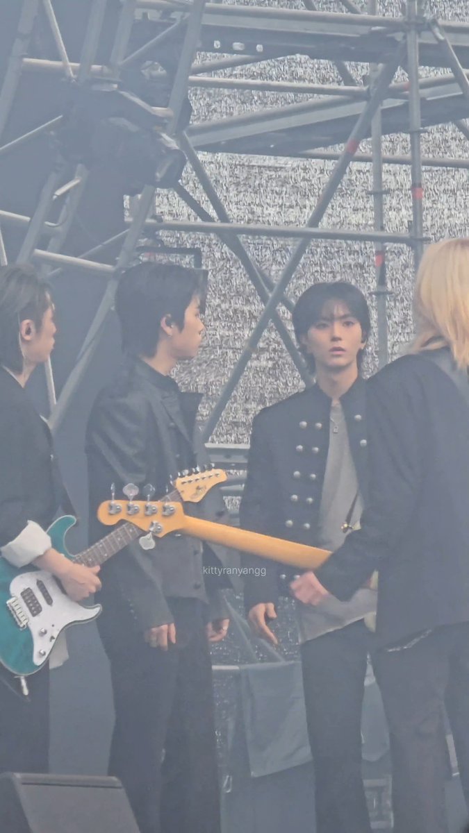 A band performing on stage, featuring members in black outfits, with one playing a teal electric guitar and another in a double-breasted jacket. A watermark 'kittyranyangg' is visible.