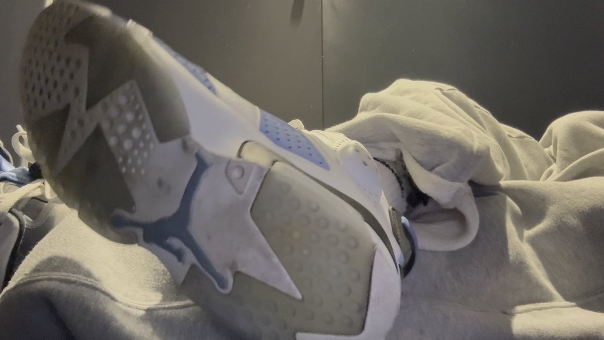 A white and blue Air Jordan sneaker is photographed in close-up resting on what appears to be a light-colored hoodie or fabric, with no visible text in the image. The caption suggests the photo depicts a playful moment with a puppy, though no puppy is visible in the frame—the image focuses entirely on the shoe, which aligns with the post's hashtags emphasizing white socks and sneaker culture.
