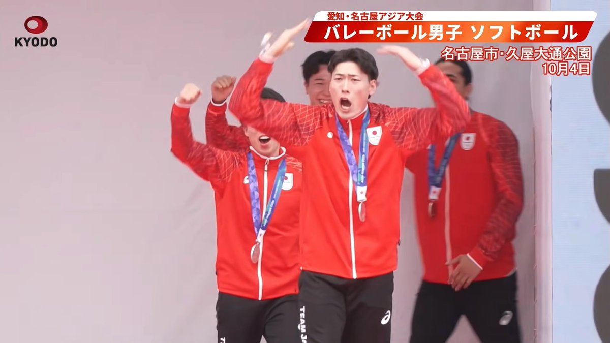 Japanese athletes wearing red Team Japan tracksuits and silver medals celebrate enthusiastically at a medal ceremony, with the on-screen text identifying the event as "愛知・名古屋アジア大会 バレーボール男子 ソフトボール 名古屋市・久屋大通公園 10月4日" (Aichi-Nagoya Asia Games, Men's Volleyball and Softball, Nagoya City Hisaya Odori Park, October 4th).

The image relates to the post as it captures the moment Japan's men's softball team received their silver medals, prompting the commenter's exaggerated, jokingly melodramatic reaction to the "Nishimoto" silver medal finish.