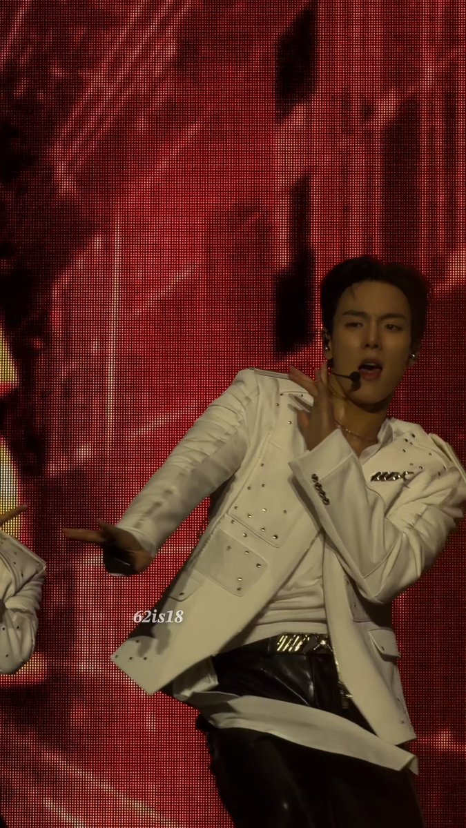 A male performer in a white embellished jacket sings on stage with a red LED screen behind him, with watermark '62is18'.