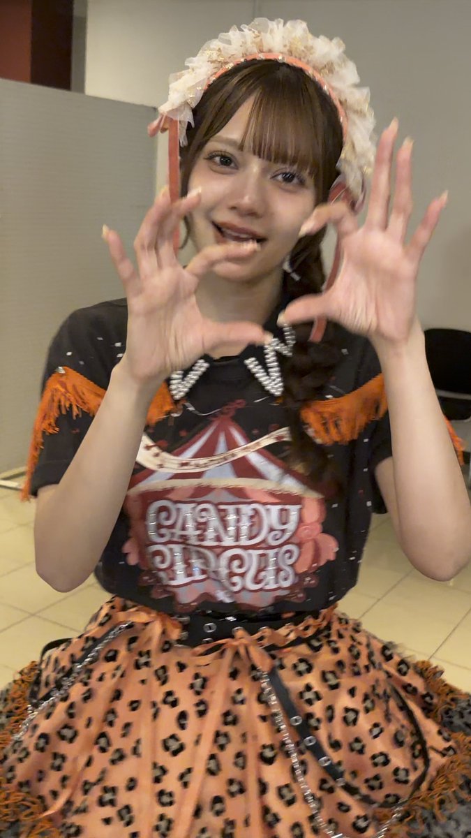 A young woman in a circus-themed outfit with a 'CANDY CIRCUS' shirt, leopard print skirt, and ruffled headpiece, smiling and holding her hands up in a claw gesture.