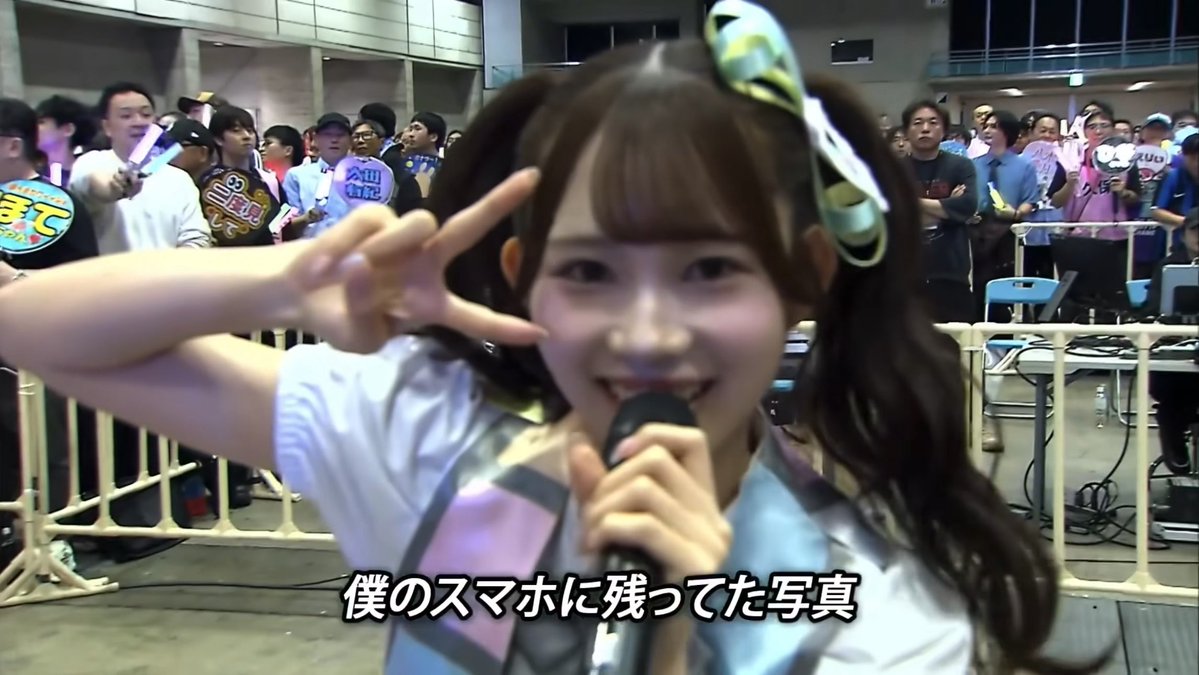 A young woman in twin tails makes a peace sign while holding a microphone at what appears to be a fan event, with Japanese subtitles reading "僕のスマホに残ってた写真" (a photo that was left on my phone). The image directly relates to the post's sentiment, showing the empty "audience side" view—likely disappointing to the speaker, who appears to be a fan or performer on stage looking out at the sparse crowd behind her.