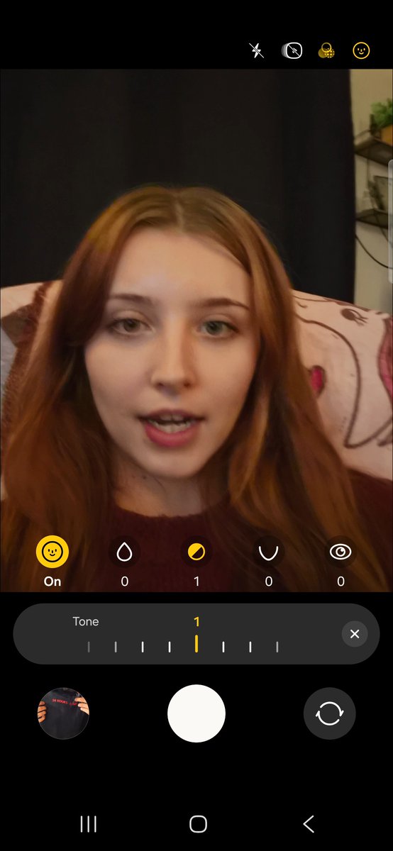 A selfie taken through a phone camera app, showing a young woman with long red hair and a camera interface with Tone adjustment set to 1.