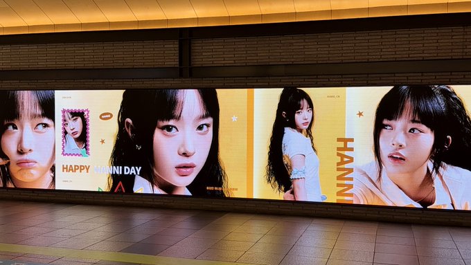 An illuminated billboard displays promotional photos of K-pop member Hanni, with visible text reading 'HAPPY HANNI DAY' and her name.