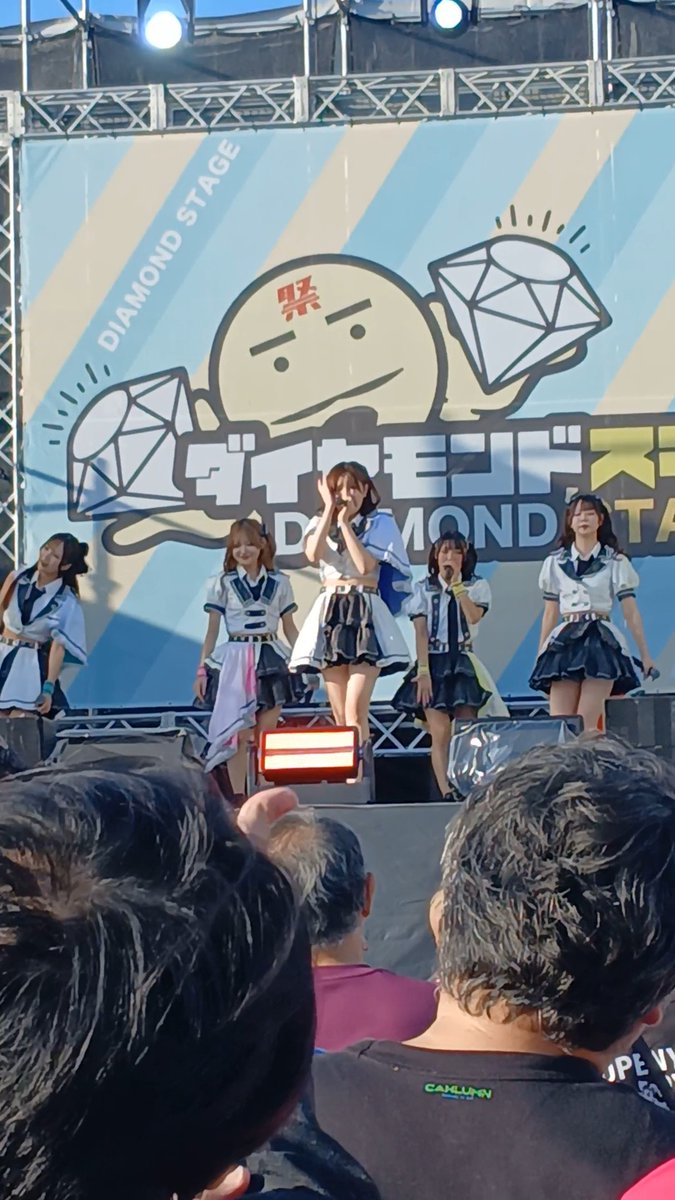 A group of female performers in sailor-style idol outfits perform on stage at the 'Diamond Stage' during the 'Diamond Tokio' idol festival event.