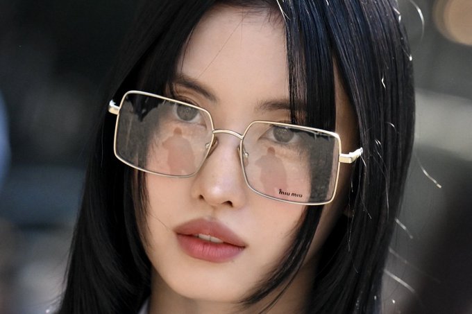 Close-up portrait of a young woman with long dark hair wearing gold-rimmed Miu Miu glasses