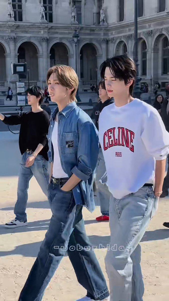 Two young men walking in front of a classical European building, one wearing a denim jacket and the other a white 'CELINE PARIS' sweatshirt, with watermark 'roborhythm'.