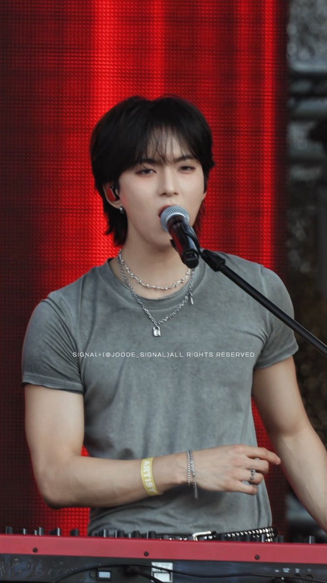 A young man with dark hair singing while playing a keyboard, wearing a gray t-shirt and silver necklaces, with a watermark 'SIGNAL▶(@JOODE_SIGNAL)ALL RIGHTS RESERVED'.