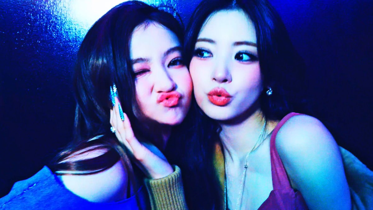 Two young women pose cheek-to-cheek, both making playful pouting lips while bathed in moody blue lighting, with sparkly nail art and bold makeup complementing the dramatic, glamorous atmosphere that matches the excited caption "ANNA & ELLA OH MY GOD."