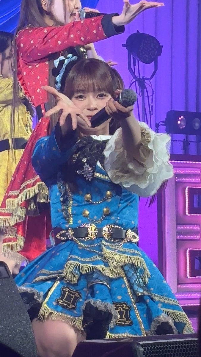A woman performing on stage in an elaborate blue and gold costume with fringe details, holding her hand out while holding a microphone.