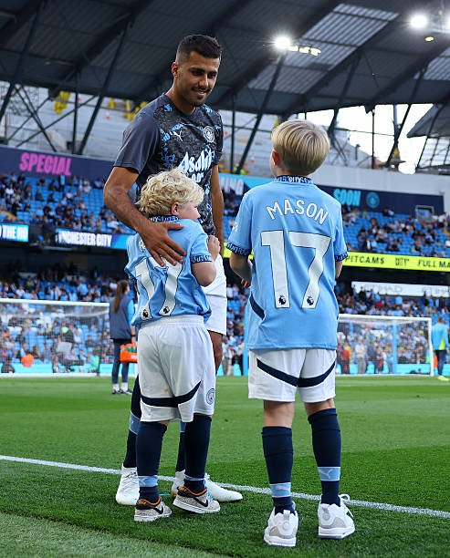 DeeTriumph's tweet photo. Rodri was so happy to see Kevin De Bruyne’s children, Romeo and Mason. 🥹🩵

Before walking out for warm-up, he played with them. After the warm-up, Mason raised his hand for Rodri to meet it — just like Rodri and De Bruyne used to do as substitutes. 😭

Mason is representing his father. 🩵

Rodri: “Mason, over to you now. Go and do it like your father.” 😂🩵