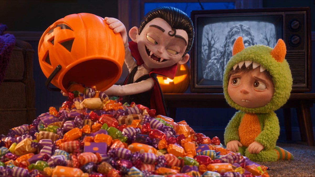 An animated scene shows a vampire character in a cape pouring a massive pile of Halloween candy from a jack-o'-lantern bucket while a child in a green monster costume watches sadly.
