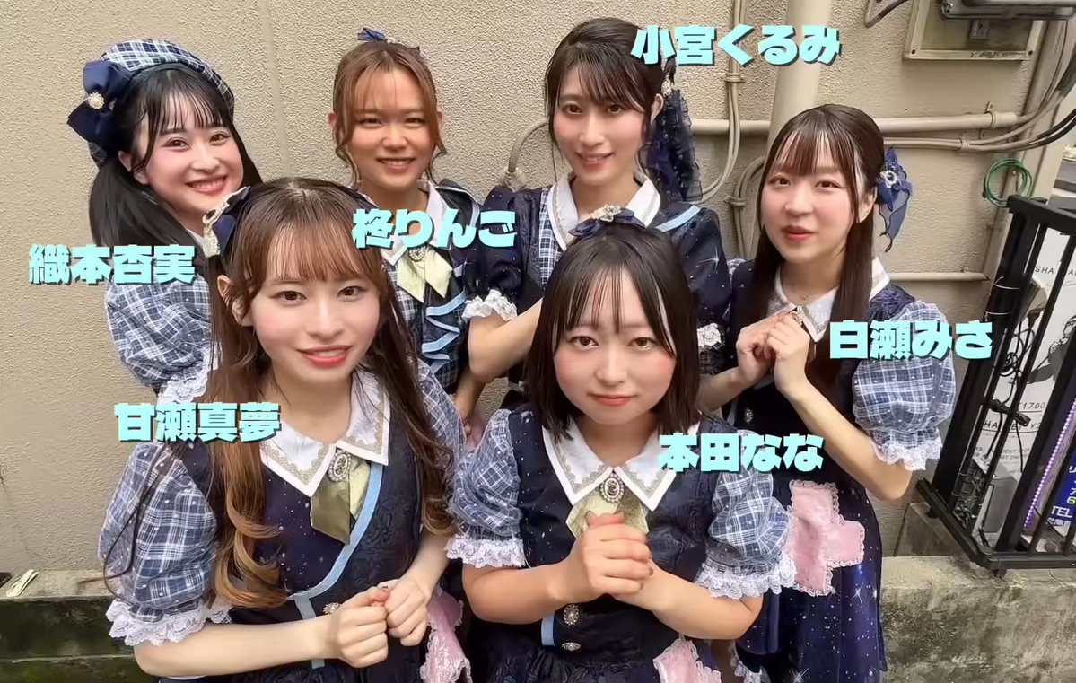 A group photo of six smiling girls in matching blue and white idol outfits with name labels in Japanese identifying each member, including "白瀬真夢" and "本田なな".