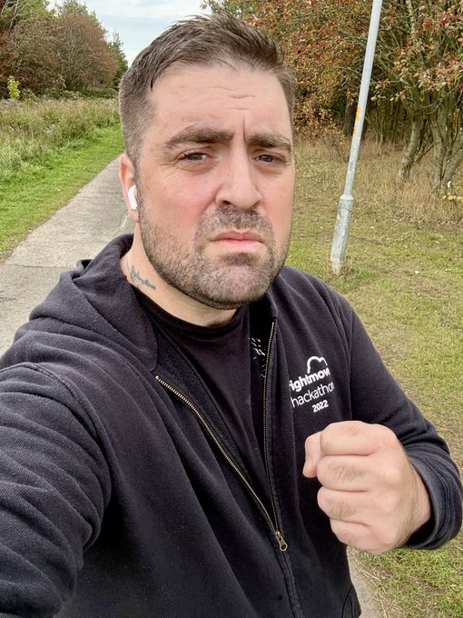 A selfie of a man wearing a black hoodie that says 'rightmove hackathon 2022', with wireless earbuds, standing on a sidewalk.