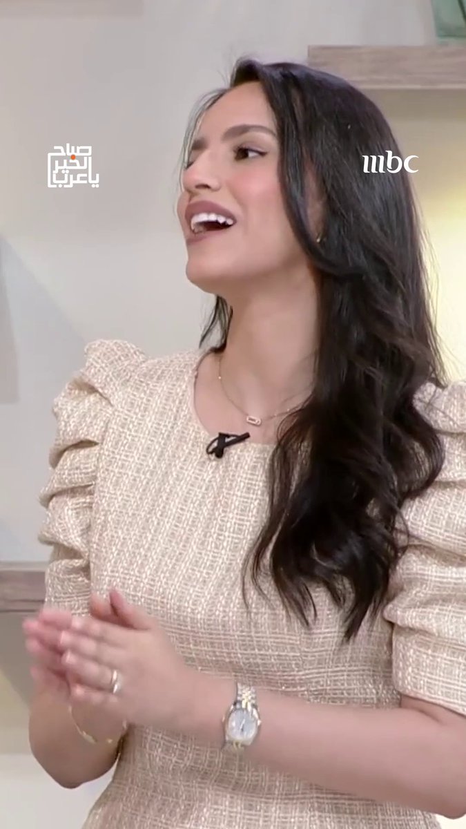 A smiling woman with long dark wavy hair wears a beige textured dress and a silver watch, appearing on an MBC television program.