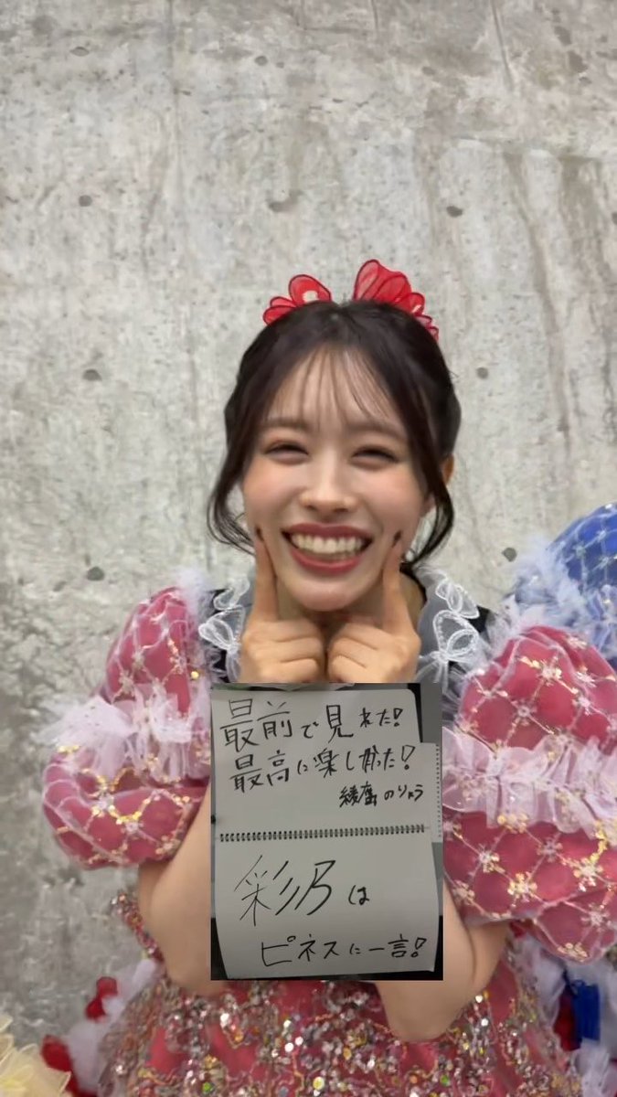 A cheerful young woman with a red bow smiles brightly while holding a handwritten sign that reads "最前で見れた！最高に楽しめた！練習のノルマはピネスに一言！" (Got to see from the very front! Had the best time! Practice homework - one word to Pinnes!), her joyful pose complementing the post's caption "両思いだね" (It's mutual love).