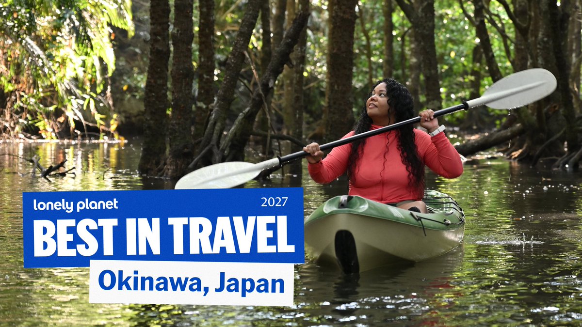 A woman in a red top kayaks through a lush mangrove forest, holding a paddle across her shoulders. The image features "Lonely Planet BEST IN TRAVEL 2027" and "Okinawa, Japan" text, promoting the destination's natural beauty as highlighted in the accompanying post.