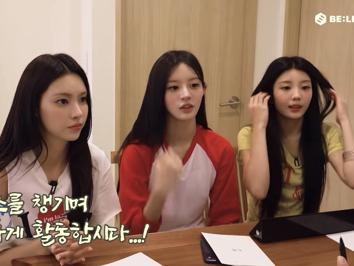 Three young women with long dark hair sitting at a wooden table, appearing to be in a video or interview setting with a 'BE:LIFT' logo in the top right and Korean subtitles at the bottom.