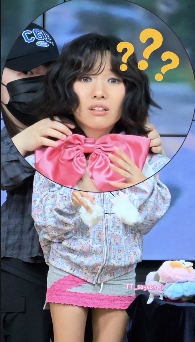 A woman wearing a pink bow and pastel patterned jacket appears confused, indicated by large question marks drawn above her head.