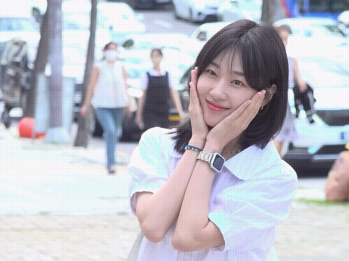 A young woman with shoulder-length dark hair smiles gently at the camera, her hands framing her cheeks, wearing a light blue collared shirt and a silver watch. The "#하윤경" caption suggests this is Ha Yoon-kyung, with the image reflecting a tender, nostalgic expression that aligns with the post's musing about perhaps being a burden to her younger self.