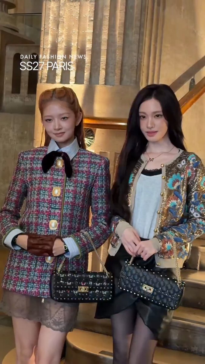 Two young women posing together on a staircase at a fashion event, labeled 'DAILY FASHION NEWS SS27 PARIS', wearing tweed Chanel outfits and carrying black studded handbags.