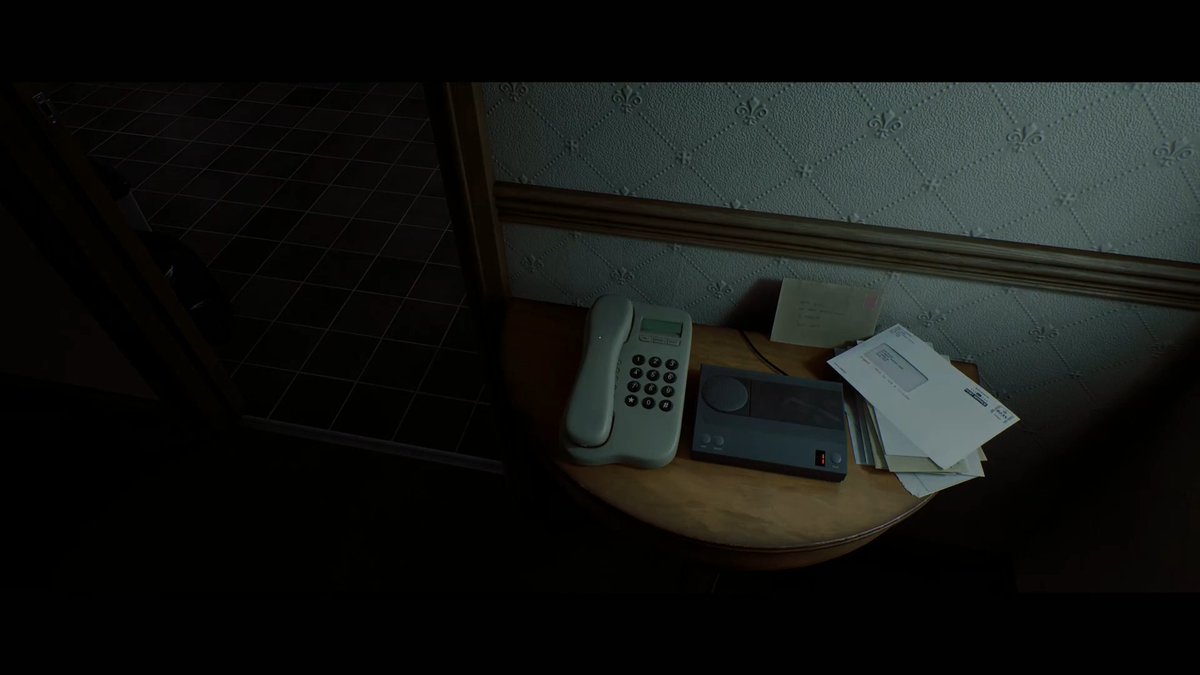 A dimly lit scene shows a vintage-style corded telephone, a small device, and a stack of papers/envelopes on a wooden side table against patterned wallpaper.