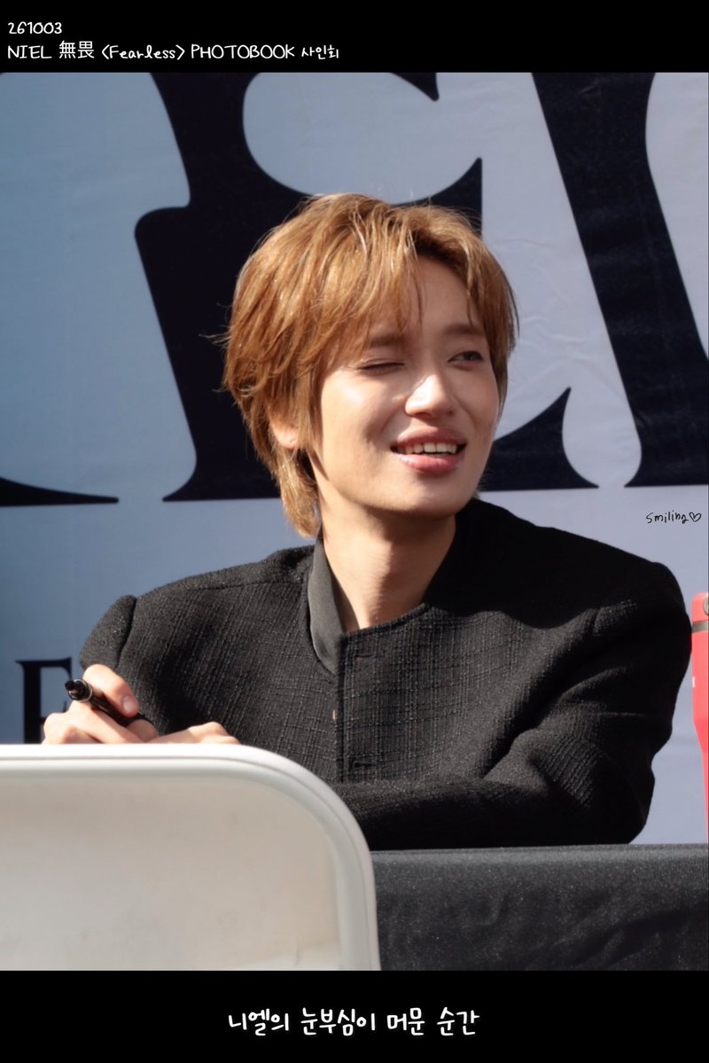 A fan-made photo of K-pop artist NIEL from the group TEENTOP smiling at what appears to be a fansign event for his 'FEARLESS' Photobook, with Korean text reading '니엘의 눈부심이 머문 순간' (The moment NIEL's radiance stayed).
