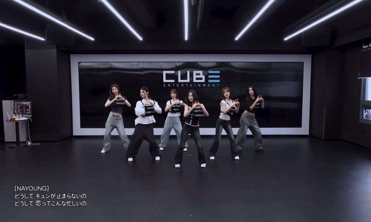Six female dancers performing a choreographed routine in a dance studio with a large 'CUBE ENTERTAINMENT' sign in the background.