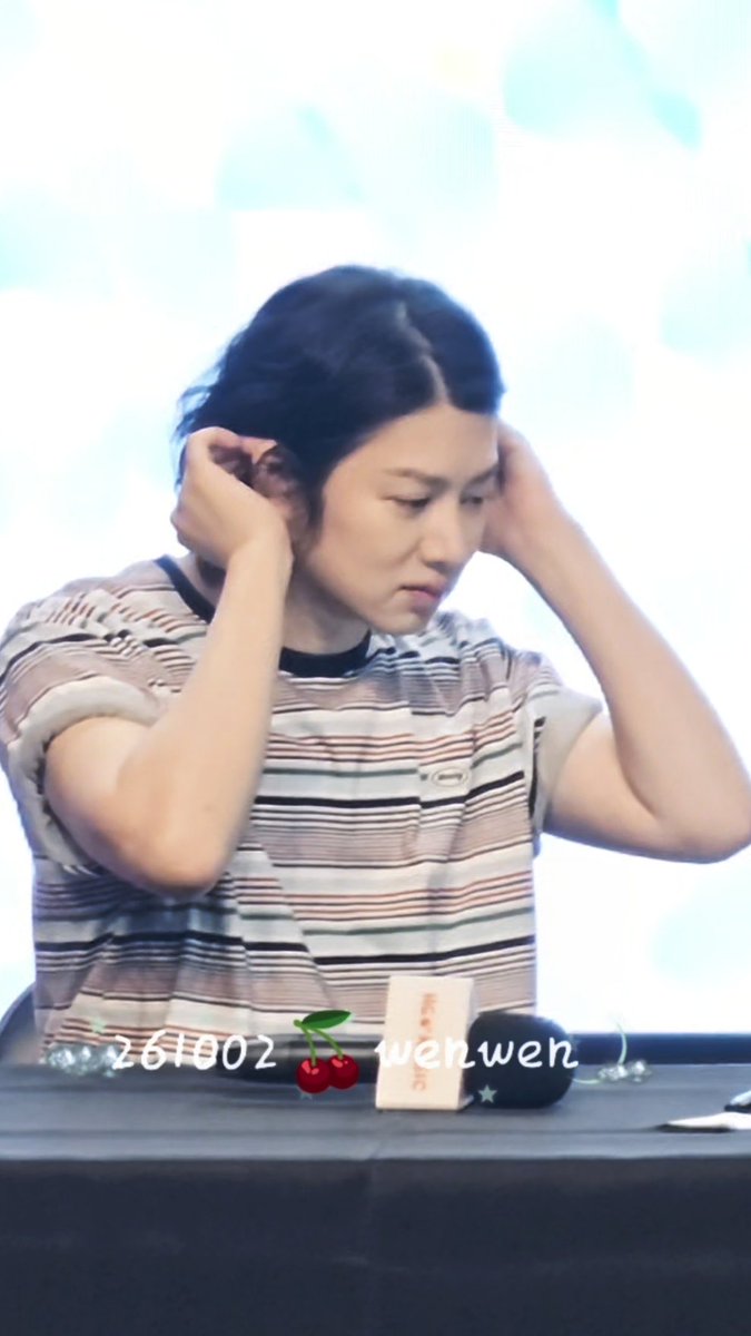 A woman in a striped shirt is shown with both hands raised to her ears, looking downward with a focused expression. A watermark reads '261002 [cherry emoji] wenwen' at the bottom.