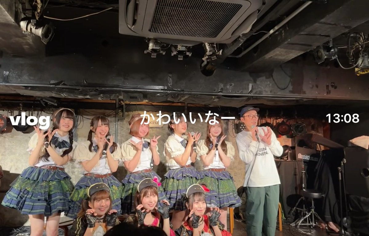 A group of six young women in matching schoolgirl-style idol costumes posing on stage with a male host, overlaid with text 'vlog', 'かわいいなー', and '13:08'.