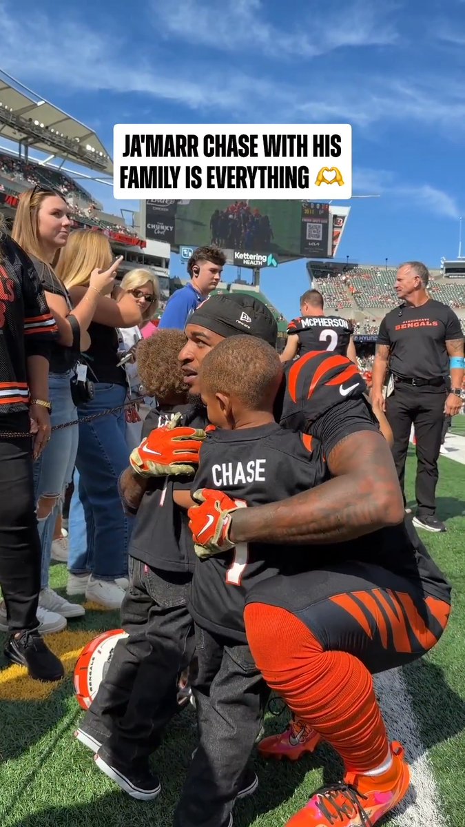 Ja'Marr Chase kneels on the field in his Bengals uniform (#1), sharing a tender embrace with two young children, with a caption overlay reading "JA'MARR CHASE WITH HIS FAMILY IS EVERYTHING." The image captures a heartfelt family moment that ties into the post's "Football is family" theme ahead of the JAXvsCIN game at 1pm ET on CBS/Paramount+.