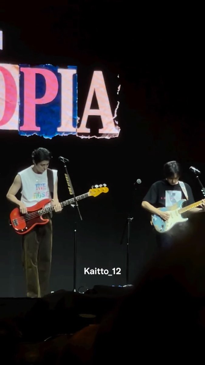 Two guitarists performing on a dark stage with 'OPIA' displayed in large letters above them; one plays a red bass guitar while the other plays a light blue electric guitar, with 'Kaitto_12' watermark.