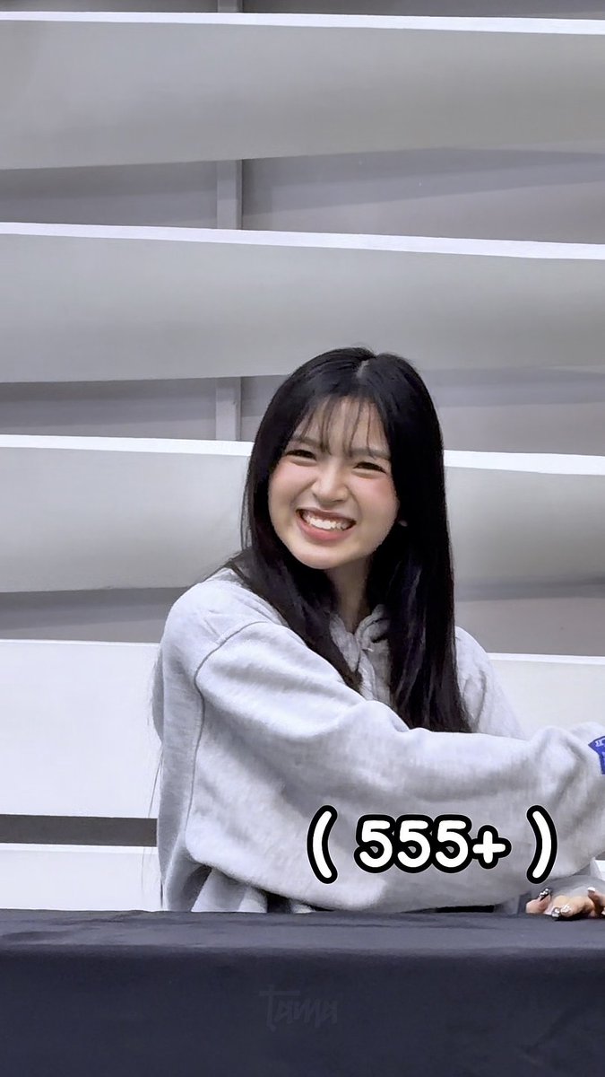 Woman with long dark hair smiling broadly while wearing a grey sweatshirt, with "( 555+ )" text overlay.
