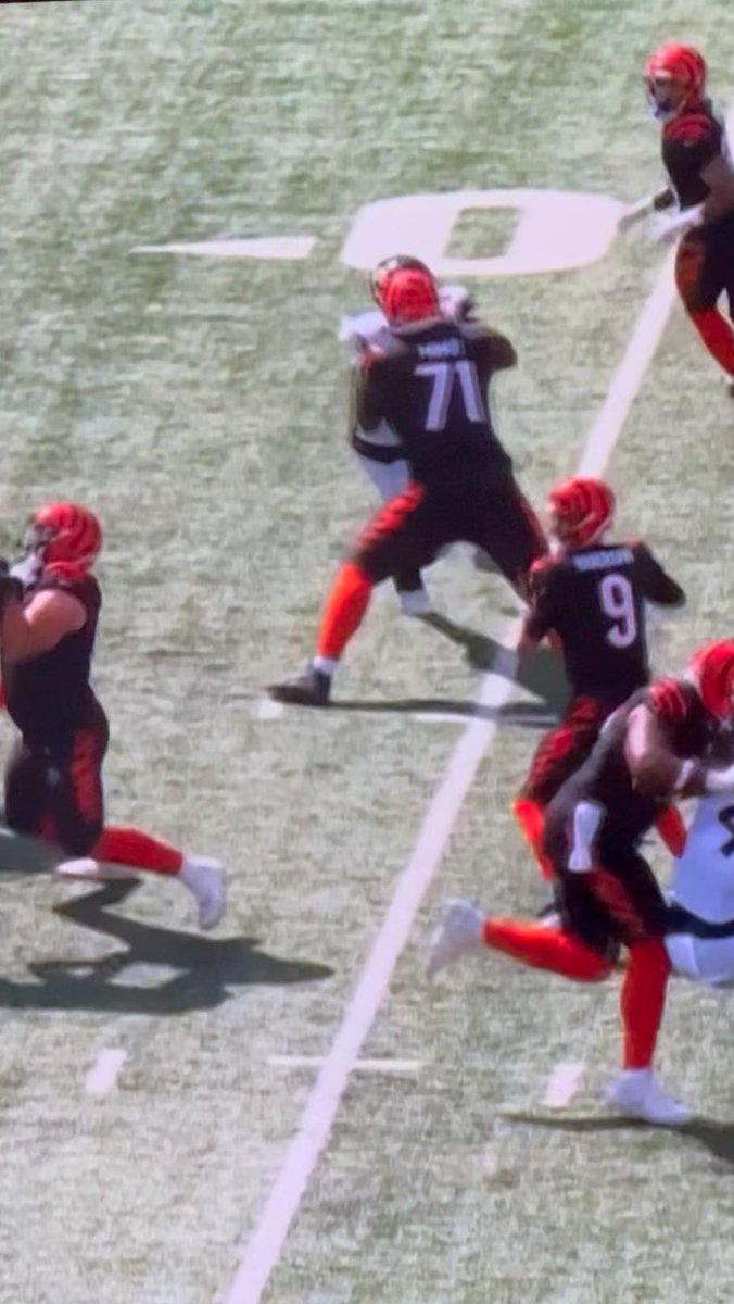 Cincinnati Bengals quarterback Joe Burrow, wearing jersey #9, stands in the pocket as his offensive lineman #71 is driven backward into him by a pass rusher. The image captures the chaotic moment of pressure breaking down, illustrating the brutal sequence that leaves Burrow vulnerable to taking a massive hit.