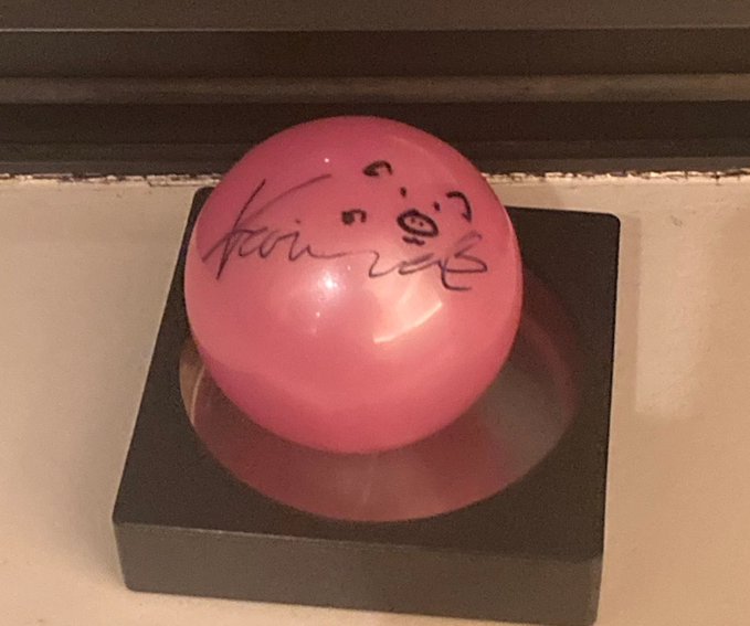 A pink, spherical ball with a signature written on it sits on a black square base.