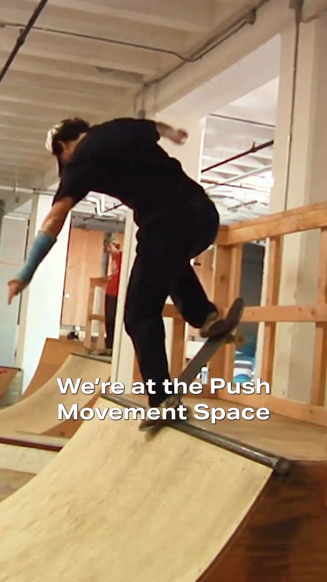 A person in dark clothing skateboards on a wooden half-pipe ramp in an indoor space, with text overlay reading 'We're at the Push Movement Space'.