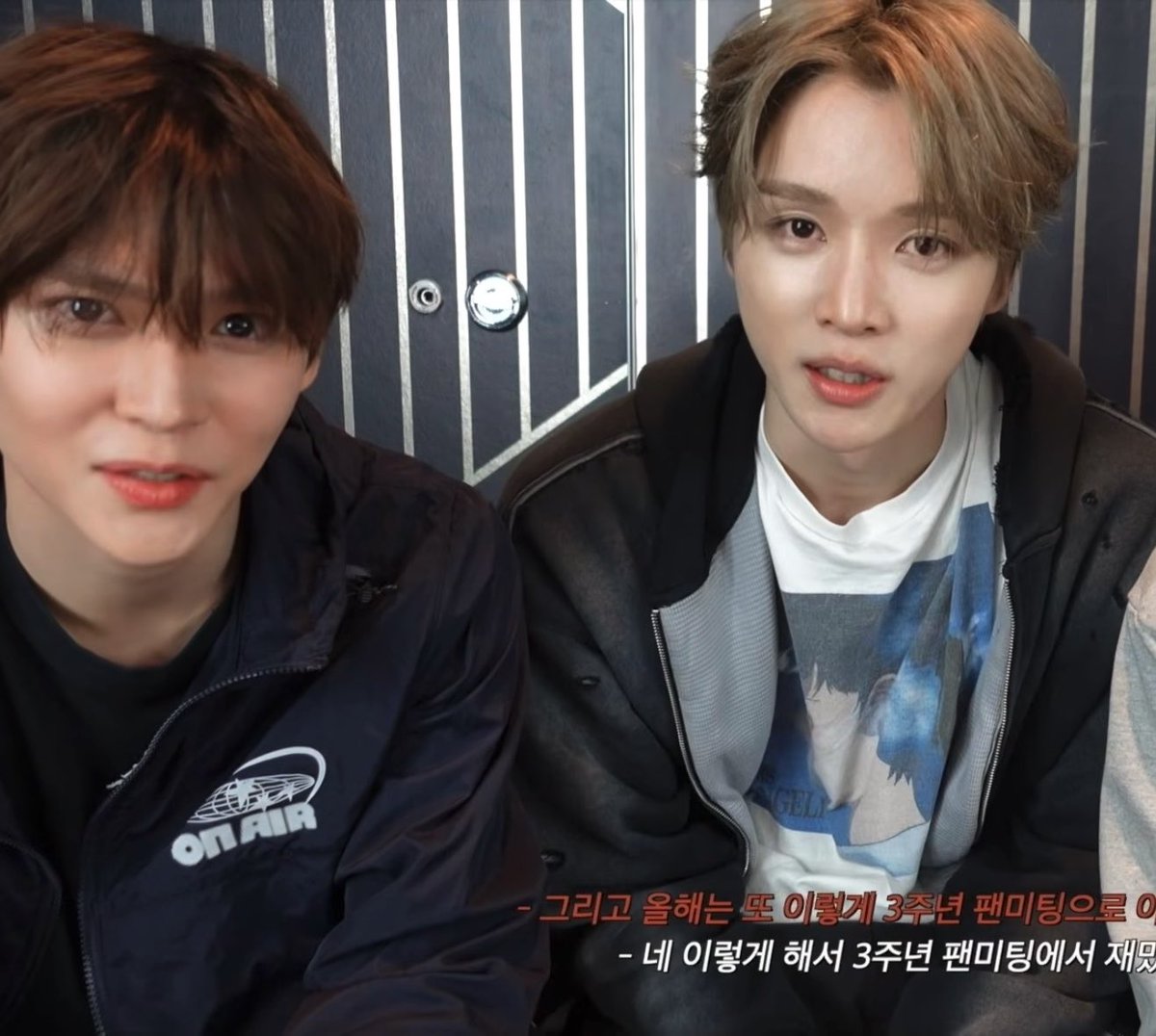 Two young men pose closely together for a selfie-style photo, both wearing dark jackets, with Korean subtitles visible at the bottom of the screen.