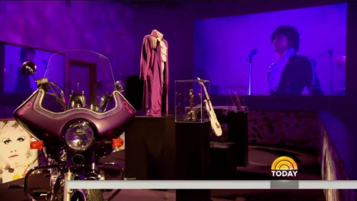 HoldOn2YourWigs's tweet photo. #PrinceOnThisDay

On the morning of October 5, 2016, the day before Prince’s @PaisleyPark was due to open to the public, Al Roker walked the halls of a place almost no outsider had ever seen.
@prince had died that April of an accidental painkiller overdose. The white compound in Chanhassen, Minnesota — studio, stage, and home since the late 1980s — had stayed sealed. Prince’s estate had announced that the complex would become a museum, with daily tours set to begin Thursday, October 6. NBC’s Today was invited in first. Roker’s tour, aired that Wednesday morning, was the first television look inside.

The rooms had been left much as Prince left them. In Studio A, handwritten notes still sat on the music stands. Keyboards and guitars were in place in the control room, still marked with his symbol. Roker reported that Prince had been working there on a jazz album not yet released. Outside the studio, an Influence Hallway carried a mural of the artists Prince counted as his own.
The Purple Rain room held the film script, a guitar, wardrobe, and one of the motorcycles from the movie. The album had spent 24 weeks at No. 1 and sold more than 20 million copies; the room also displayed Prince’s Academy Award for the film and his 2004 Grammy for Musicology. Archivist Angie Marchese told Roker that Prince had every garment custom-made and had saved nearly all of them — about 6,000 pieces, each with matching shoes. The Purple Rain outfits were cut for a 22½-inch waist. “We do have an amazing inventory because Prince saved everything,” she said. Finding mannequins small enough was the harder job.

Prince’s private living quarters were not part of the public tour. What visitors would see, the family said, was what he had already arranged. Sisters Sharon and Norrine Nelson walked the exhibits with Roker. Sharon said he had planned the museum himself: “Everything is strategically placed. And when the fans come in they’ll see that it is.” Norrine called it “truly Prince. He thought all this through. He had a vision and he finished it.”

Later that morning, in a live interview, younger sister Tyka Nelson said she wanted guests to feel as if they had seen him up close — not from a seat, but almost face to face.

The opening itself was already in doubt. The night before, on October 3, the Chanhassen City Council had voted 3–2 to table the rezoning that would let Paisley Park operate as a museum, citing traffic, parking, and public safety. Planners had projected as many as 2,000 visitors a day. On October 4 the city granted a temporary permit for three dates only: October 6, October 8, and October 14, with guests shuttled from off-site parking. Ticket holders for other early dates were offered refunds or rebooking. A full vote was pushed to on or before December 20.

Roker’s broadcast still went out as planned, the day before those limited tours began. For a few hours on national television, the private compound was no longer private: notes on the stands, a motorcycle under museum lights, and a wardrobe Prince had never thrown away.