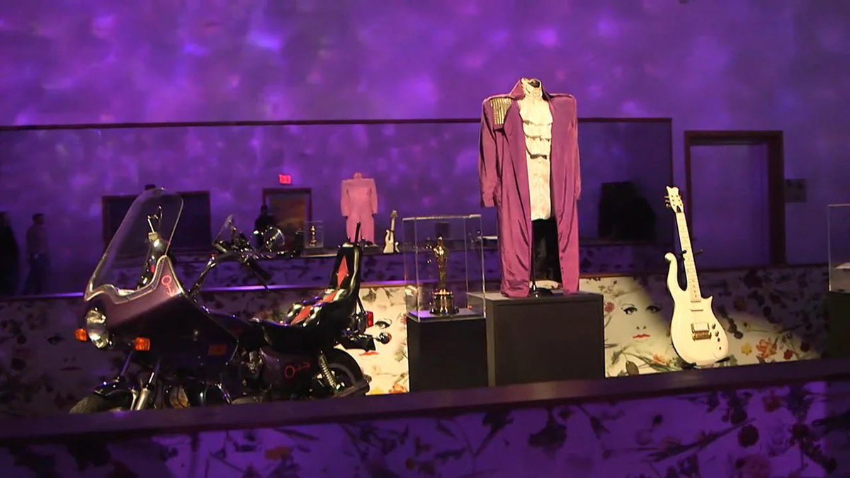 HoldOn2YourWigs's tweet photo. #PrinceOnThisDay

On the morning of October 5, 2016, the day before Prince’s @PaisleyPark was due to open to the public, Al Roker walked the halls of a place almost no outsider had ever seen.
@prince had died that April of an accidental painkiller overdose. The white compound in Chanhassen, Minnesota — studio, stage, and home since the late 1980s — had stayed sealed. Prince’s estate had announced that the complex would become a museum, with daily tours set to begin Thursday, October 6. NBC’s Today was invited in first. Roker’s tour, aired that Wednesday morning, was the first television look inside.

The rooms had been left much as Prince left them. In Studio A, handwritten notes still sat on the music stands. Keyboards and guitars were in place in the control room, still marked with his symbol. Roker reported that Prince had been working there on a jazz album not yet released. Outside the studio, an Influence Hallway carried a mural of the artists Prince counted as his own.
The Purple Rain room held the film script, a guitar, wardrobe, and one of the motorcycles from the movie. The album had spent 24 weeks at No. 1 and sold more than 20 million copies; the room also displayed Prince’s Academy Award for the film and his 2004 Grammy for Musicology. Archivist Angie Marchese told Roker that Prince had every garment custom-made and had saved nearly all of them — about 6,000 pieces, each with matching shoes. The Purple Rain outfits were cut for a 22½-inch waist. “We do have an amazing inventory because Prince saved everything,” she said. Finding mannequins small enough was the harder job.

Prince’s private living quarters were not part of the public tour. What visitors would see, the family said, was what he had already arranged. Sisters Sharon and Norrine Nelson walked the exhibits with Roker. Sharon said he had planned the museum himself: “Everything is strategically placed. And when the fans come in they’ll see that it is.” Norrine called it “truly Prince. He thought all this through. He had a vision and he finished it.”

Later that morning, in a live interview, younger sister Tyka Nelson said she wanted guests to feel as if they had seen him up close — not from a seat, but almost face to face.

The opening itself was already in doubt. The night before, on October 3, the Chanhassen City Council had voted 3–2 to table the rezoning that would let Paisley Park operate as a museum, citing traffic, parking, and public safety. Planners had projected as many as 2,000 visitors a day. On October 4 the city granted a temporary permit for three dates only: October 6, October 8, and October 14, with guests shuttled from off-site parking. Ticket holders for other early dates were offered refunds or rebooking. A full vote was pushed to on or before December 20.

Roker’s broadcast still went out as planned, the day before those limited tours began. For a few hours on national television, the private compound was no longer private: notes on the stands, a motorcycle under museum lights, and a wardrobe Prince had never thrown away.