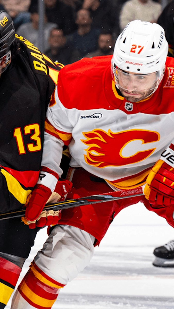 A hockey player wearing a Calgary Flames jersey (number 27, with 'TELUS' and 'Bauer' on his helmet) battles against an opponent in a black and yellow jersey (number 13) on the ice.