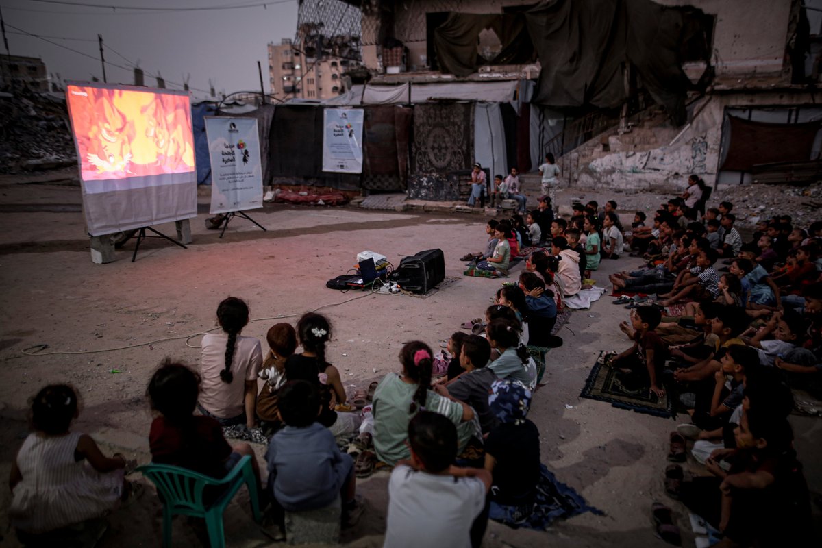 QudsNen's tweet photo. Palestinian children gather around a small makeshift screen set up among the heavy rubble of destroyed buildings in the Sheikh Radwan neighborhood of Gaza City, in the besieged northern Gaza Strip. 

📷 Saeed Jaras/Anadolu https://t.co/WWhMRygAYV