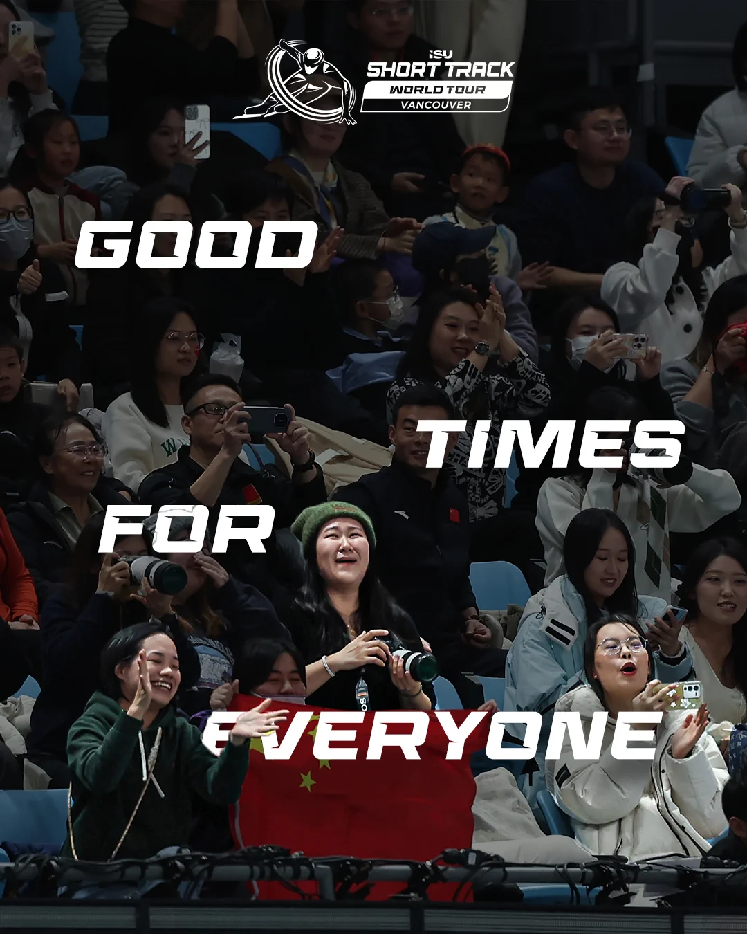 A group of enthusiastic spectators in an arena, holding cameras and phones, cheering, and waving a flag with a star design. The image features the text "Good Times For Everyone." At the top, there's a logo for the ISU Short Track World Tour in Vancouver.