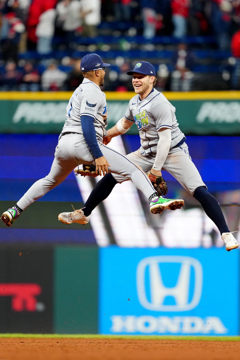 Richie Palacios and Taylor Walls leap with joy after the Rays win in Game 4 of the 2026 ALCS. They wear road gray Rays uniforms and dark blue caps.
