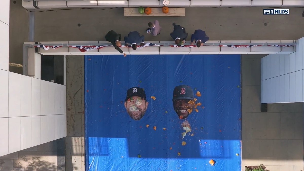 An overhead view shows a messy game show setup with a large blue tarp below a balcony, where five people stand ready to splat pumpkins and food at cutout faces of David Ortiz and Justin Verlander (identifiable by their Red Sox "B" and Detroit Tigers "D" caps). The FS1 NLDS logo appears in the corner, indicating this is from a broadcast segment where the MLB stars' faces serve as targets for the chaotic "Fact or Splat" challenge.