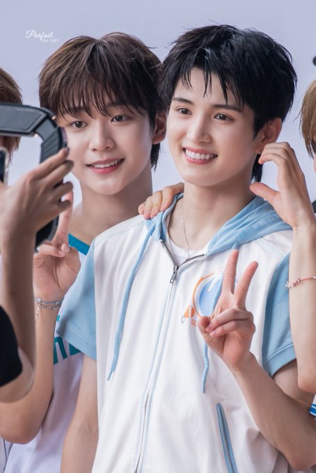 Two young men smile and make peace gestures, with one holding a phone; the image has a 'D7P' watermark in the upper left corner.